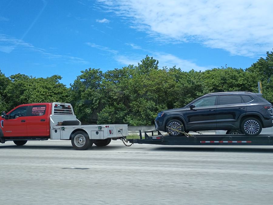D&R Auto Transport red truck towing flatbed with SUV on highway